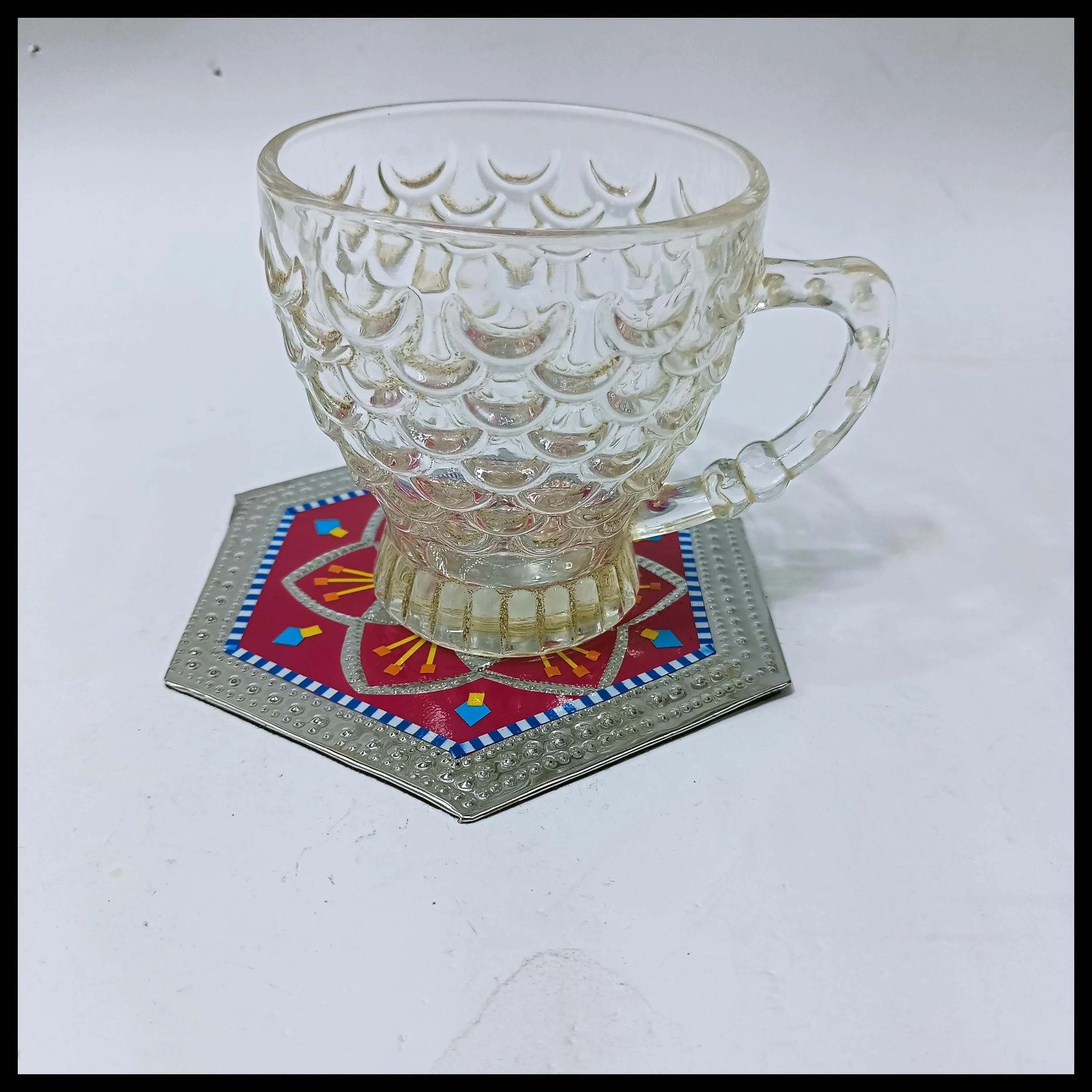 Glass tea cup placed on colorful Chamakpatti truck art coaster